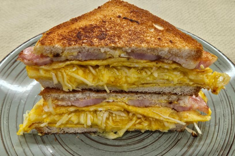 A sandwich with toasted bread, an omelet, ham, crunchy cabbage, and melted cheese, cut in half and stacked on a green plate.