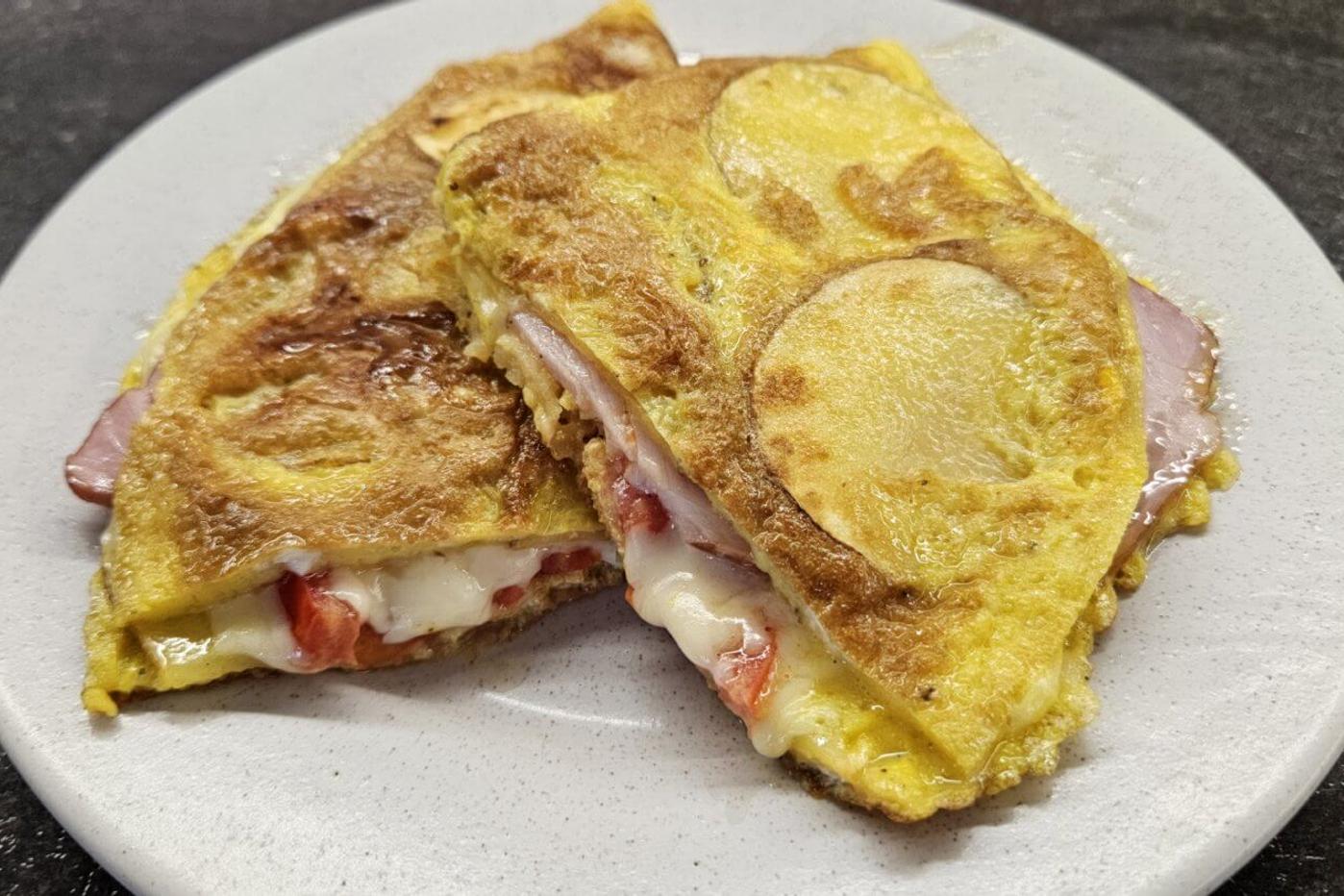 A folded omelette with tomatoes, cheese, and ham, served on a speckled off-white plate.
