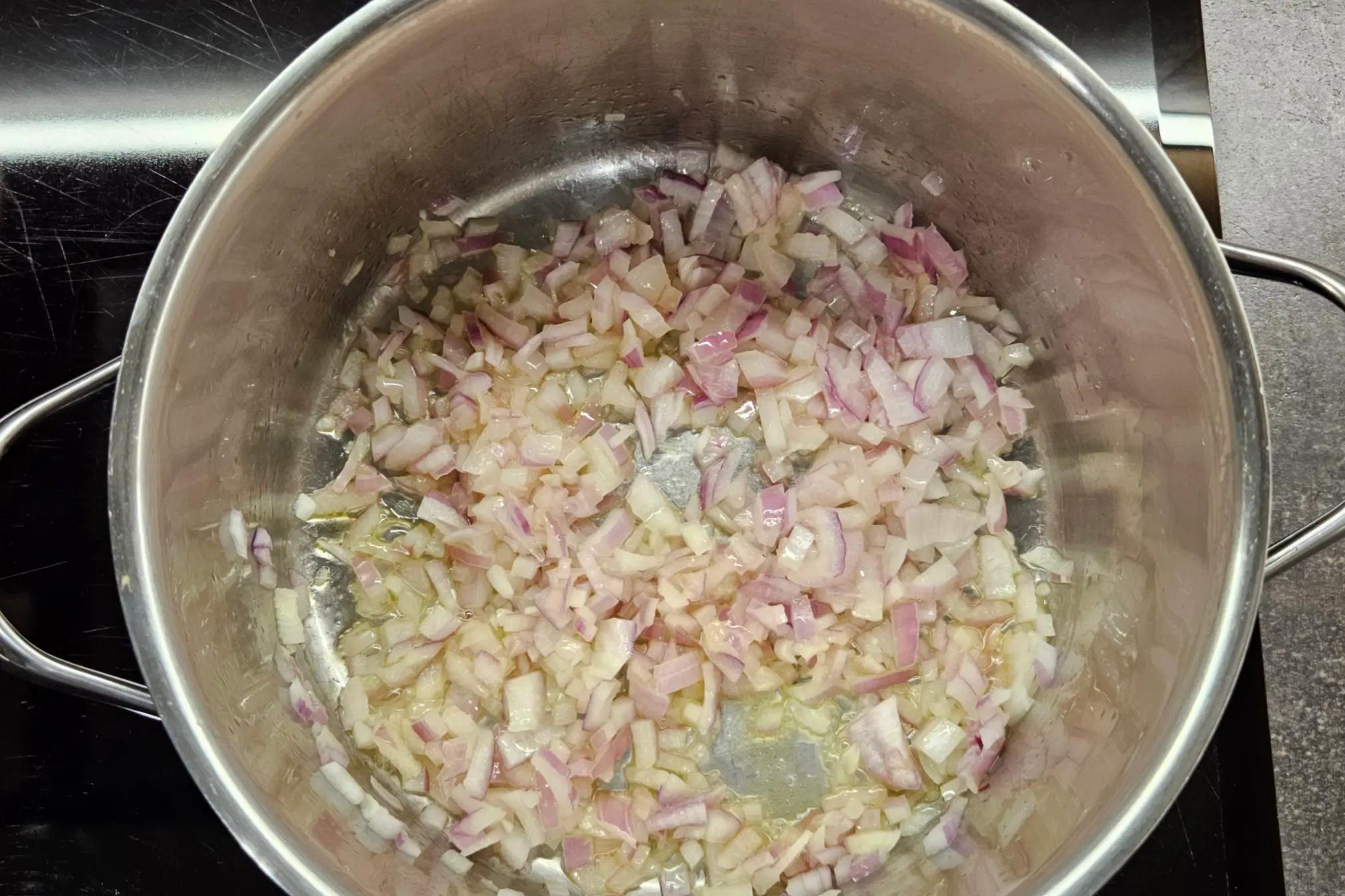 Diced red onion sautéing in olive oil at the bottom of a large soup pot.