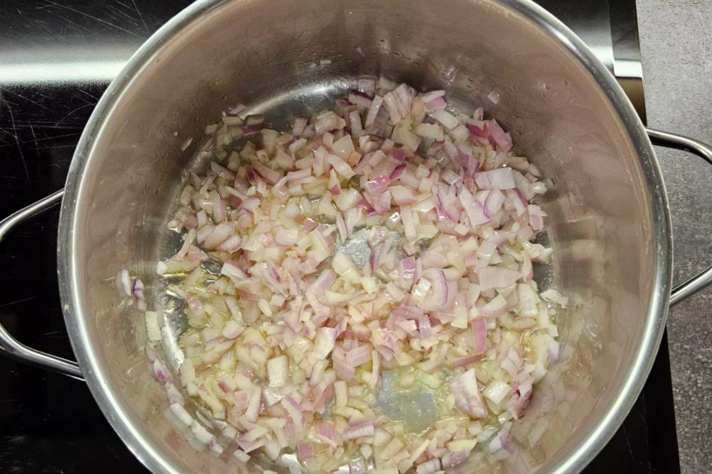 Diced red onion sautéing in olive oil at the bottom of a large soup pot.