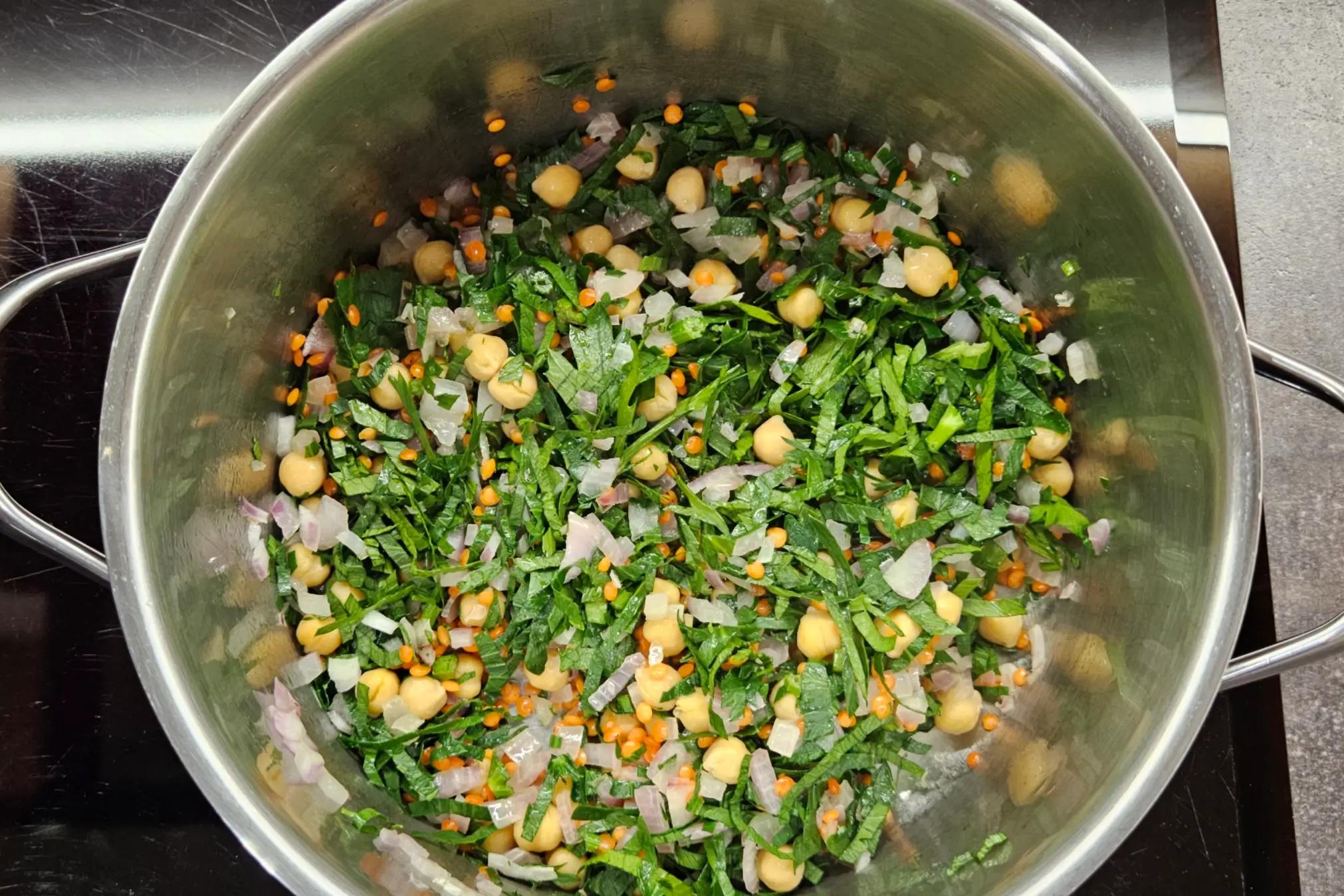 Finely chopped fresh herbs being added to the pot with sautéed onions and spices.