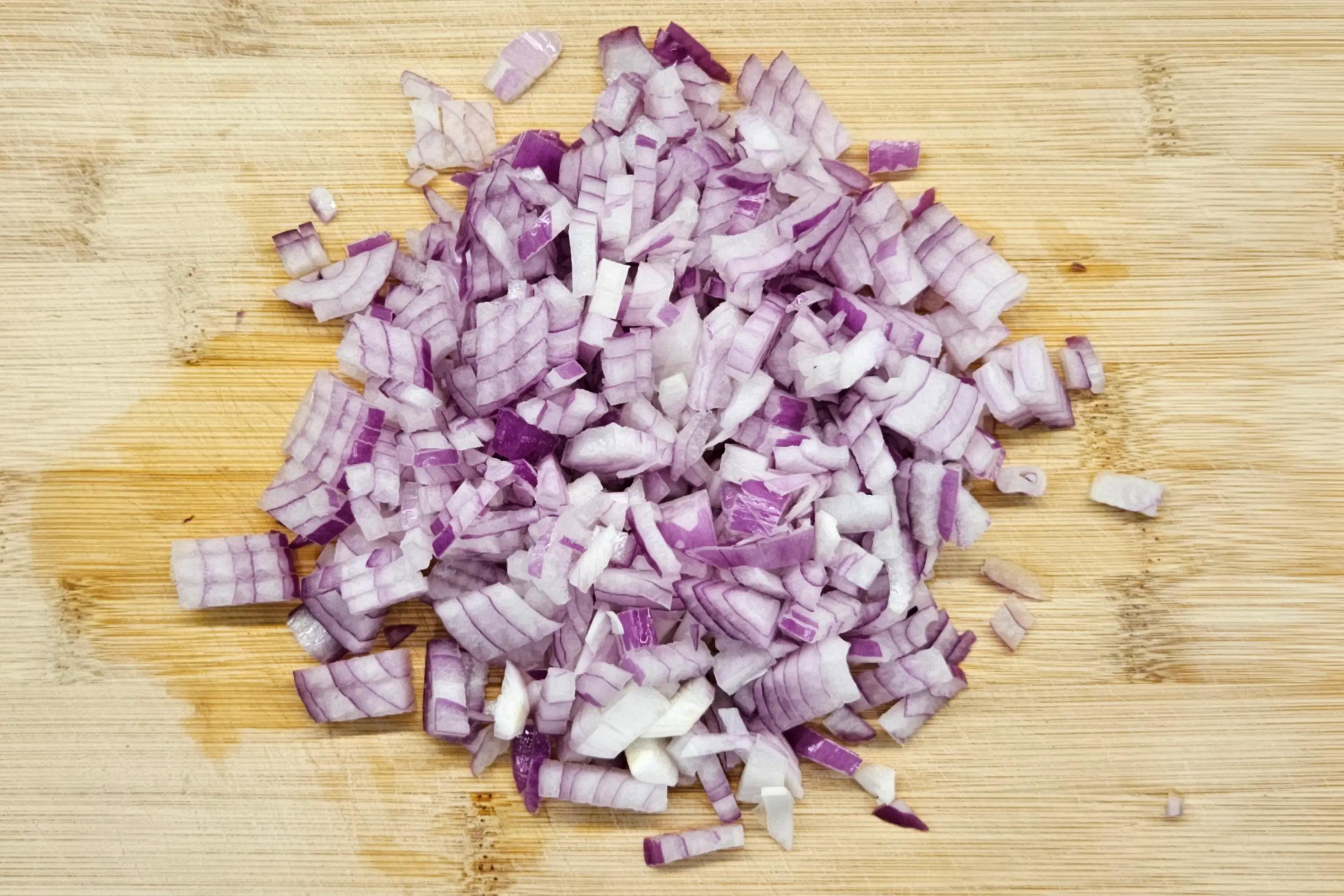 Finely diced red onion on a wooden cutting board for Harira soup preparation.