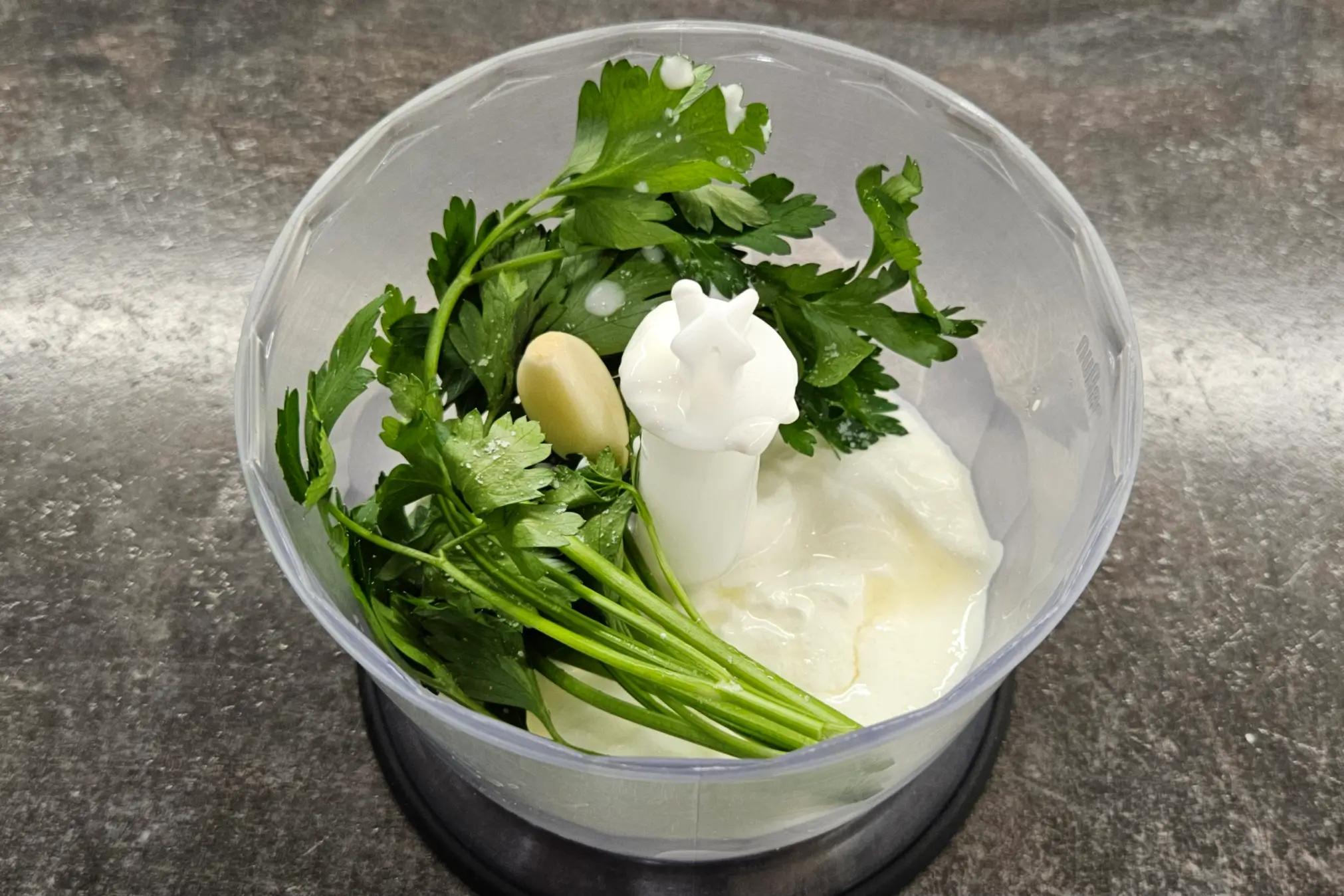 Ingredients for the green herb and garlic yogurt sauce inside a blender jar.