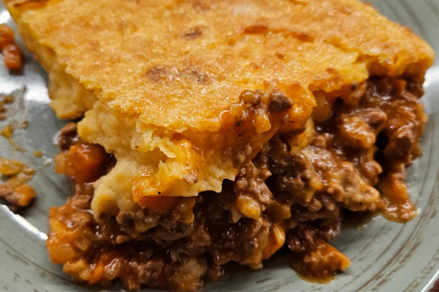 A slice of shepherd’s pie on a plate, showing layers of golden mashed potatoes and a savory meat stew with carrots and onions.