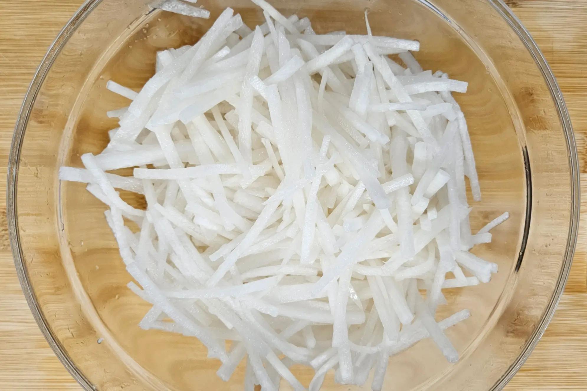 Salted daikon radish sweating in a large mixing bowl.