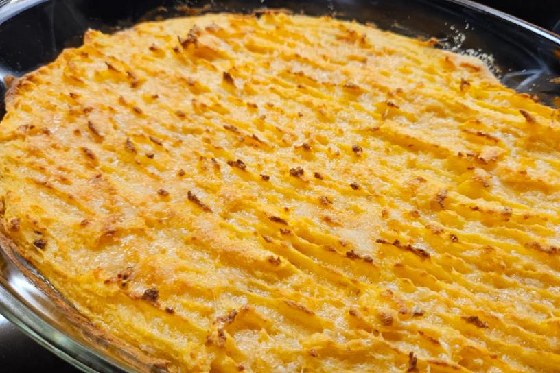 A baked shepherd’s pie in a glass dish with a golden, wavy crust topped with crisp browned ridges.