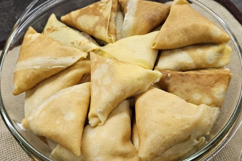 Cheese-stuffed nalysnyky, folded into triangles, arranged in a clear baking dish.