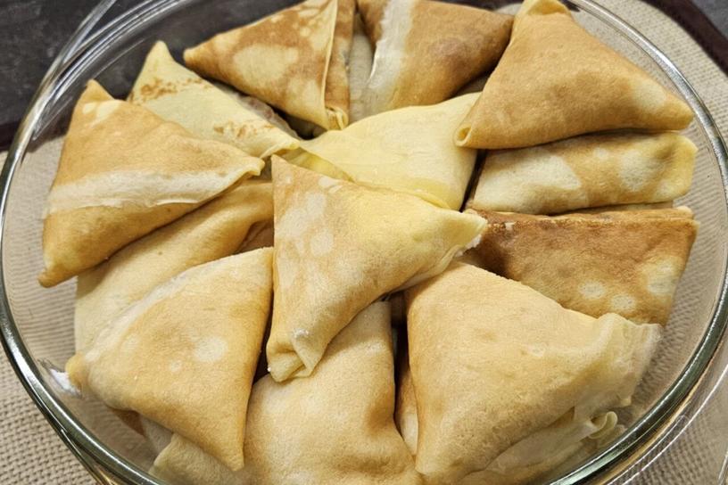 Налисники з сиром, завернуті в трикутники, викладені в прозору форму для запікання.