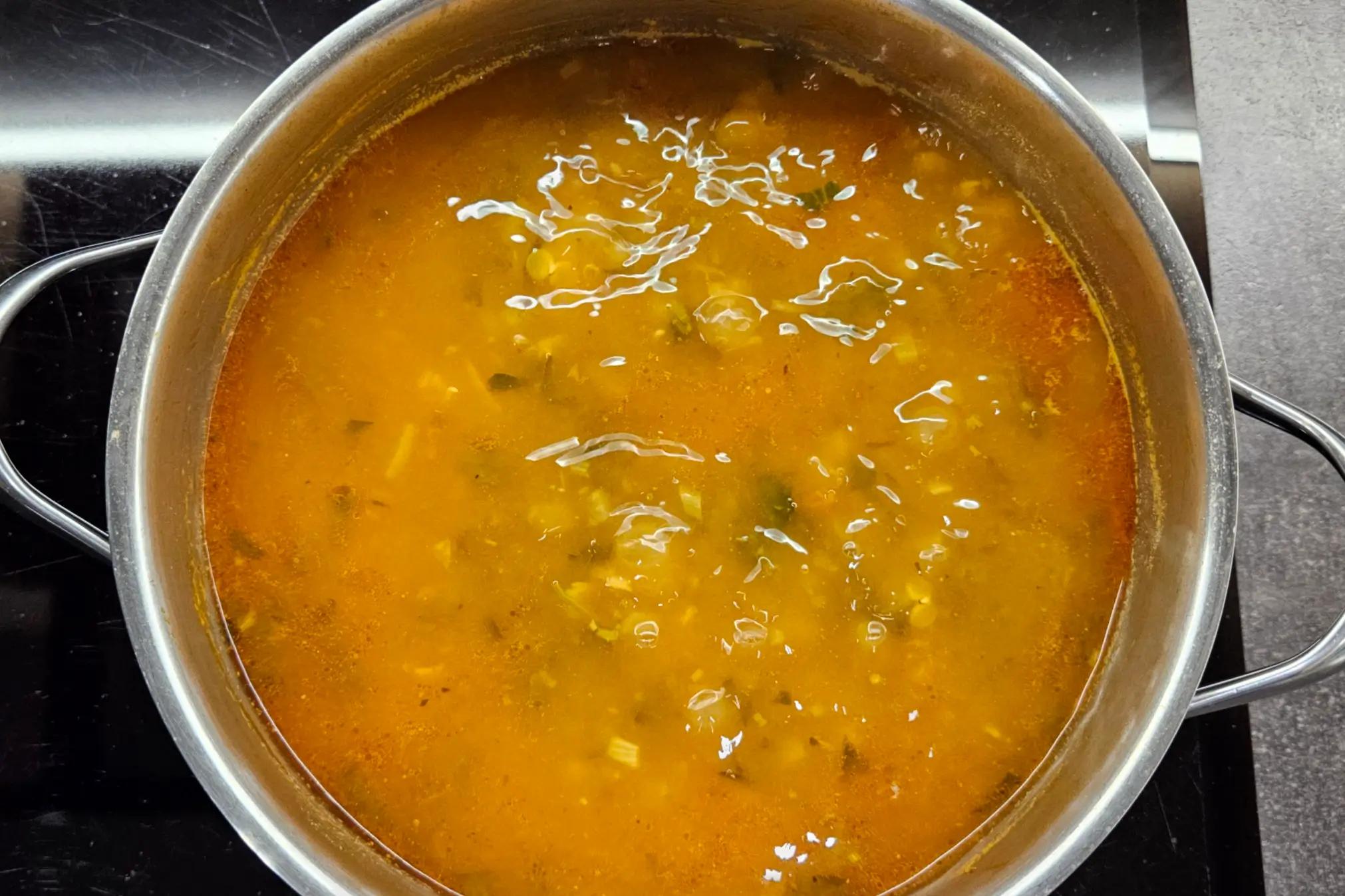 Boiling water poured over lentils, chickpeas, and tomatoes in a simmering soup pot.