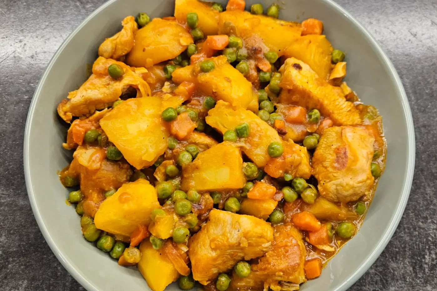 Braised turkey with potatoes and green peas in a rich tomato-based sauce, served in a bowl on a dark surface.