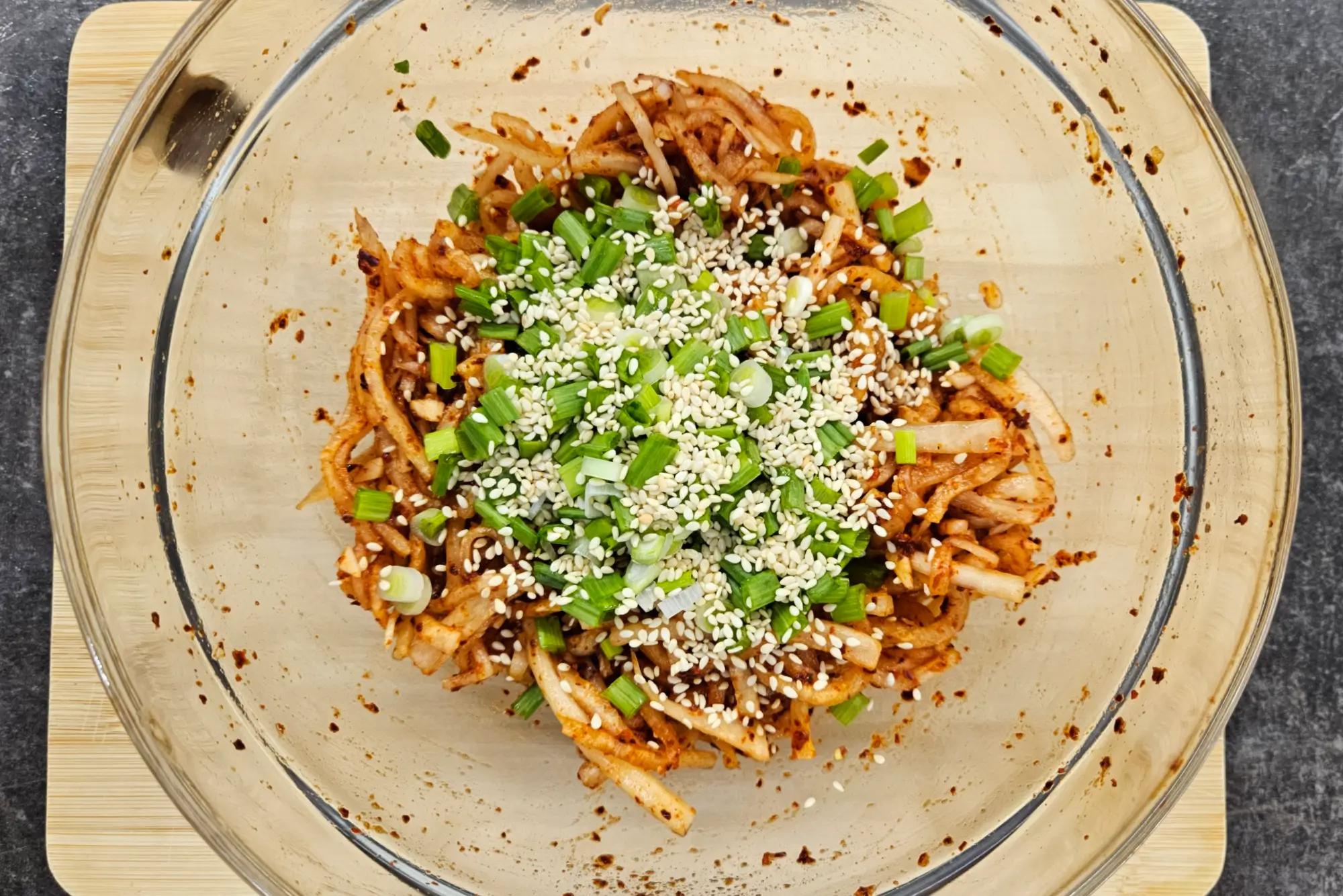 Finished Musaengchae salad garnished with toasted sesame seeds and chopped scallions.