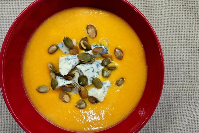 Creamy pumpkin soup served in a red bowl, topped with Dorblu cheese and sunflower seeds.