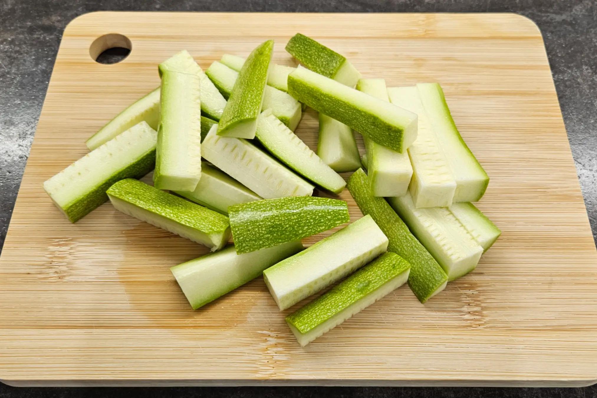Fresh zucchini cut into neat sticks on a wooden cutting board.