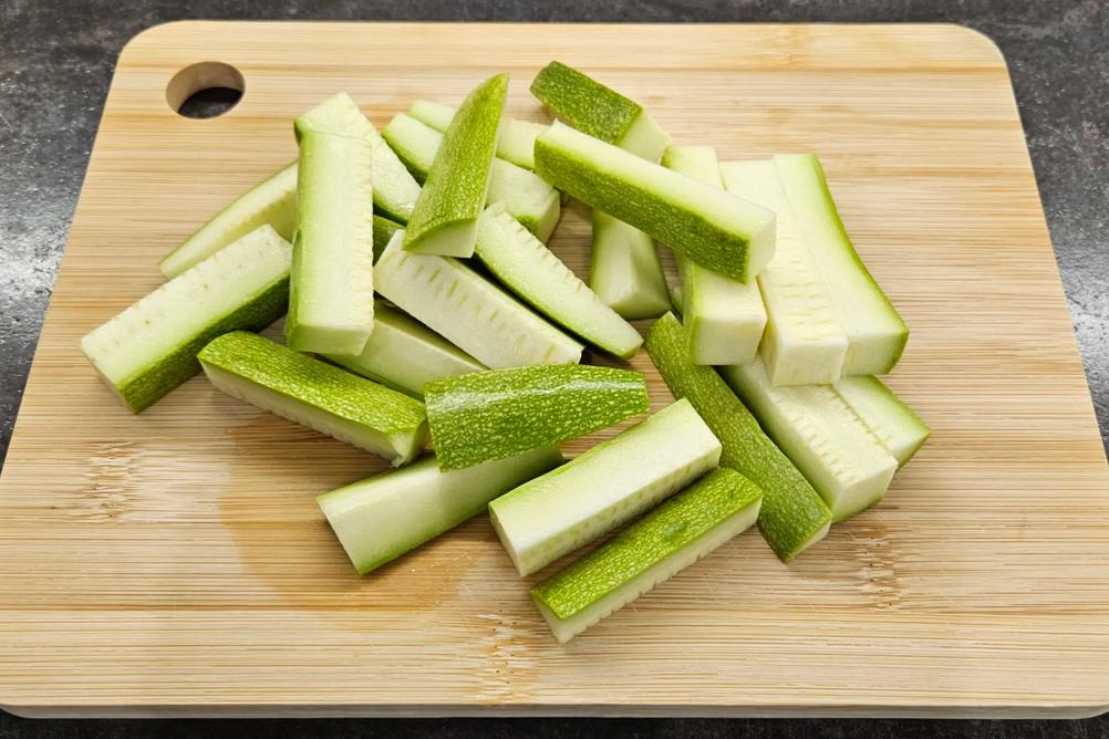 Fresh zucchini cut into neat sticks on a wooden cutting board.