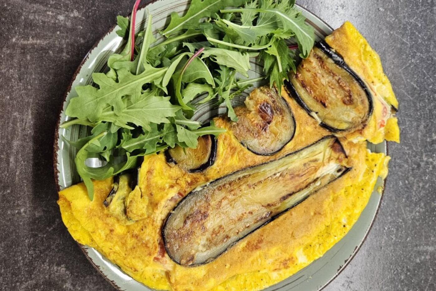 A folded omelette with eggplant, served on a green plate with a side of fresh salad leaves.