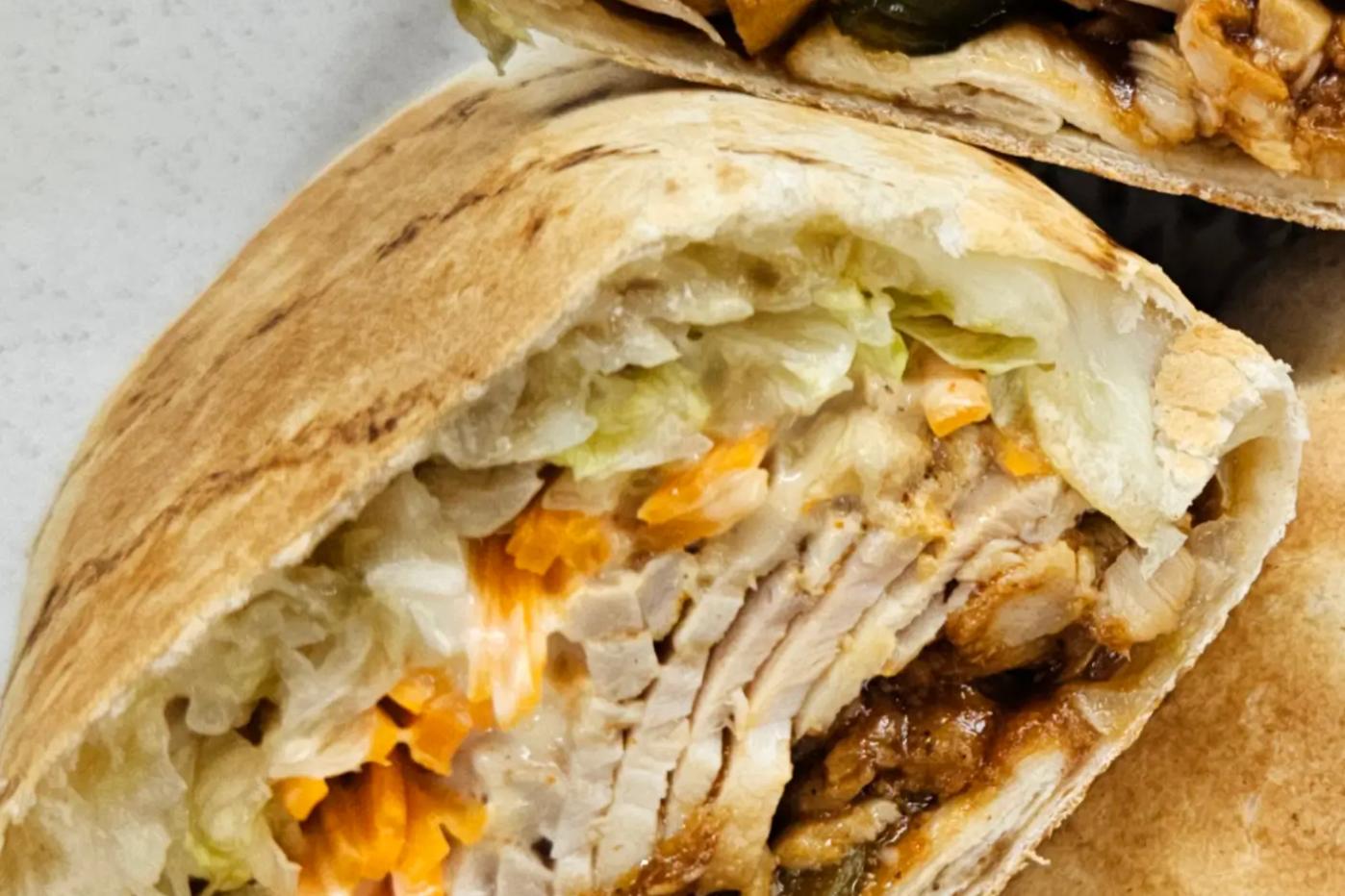 Розрізаного рулету з тортильї, наповненого соковитою куркою, тушкованими овочами, тертою морквою та салатом айсберг, загорнутого в підсмажений лаваш.