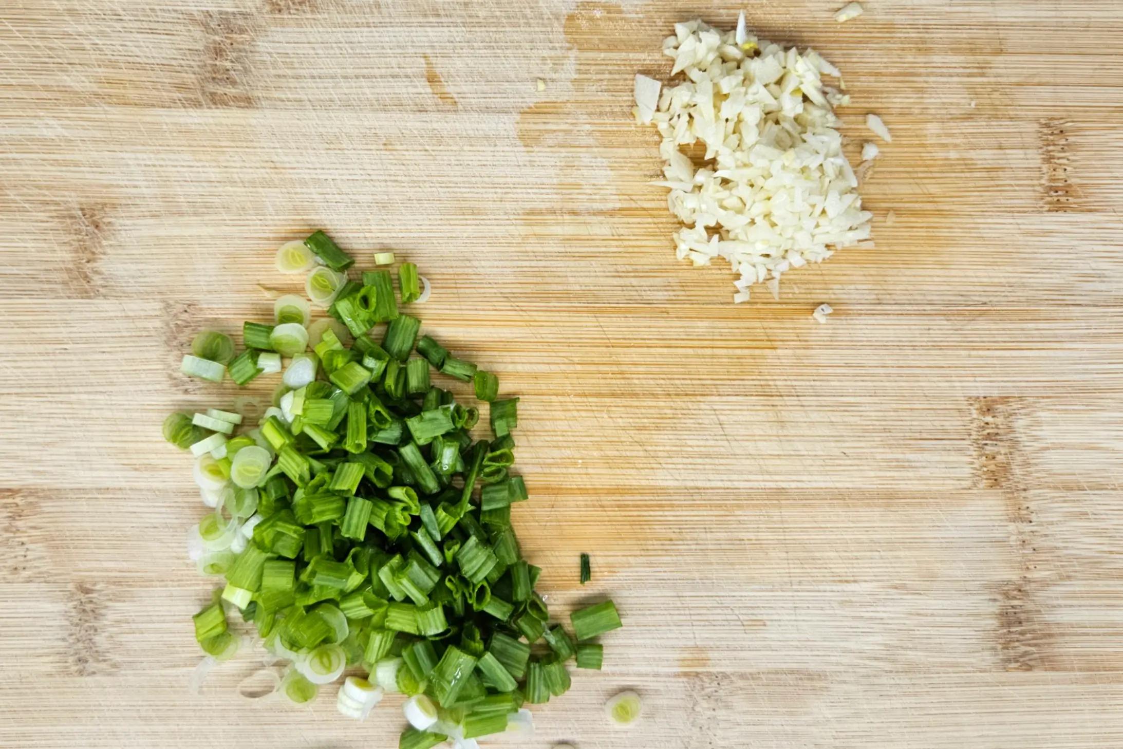 Finely chopped scallions and minced fresh garlic on a cutting board.