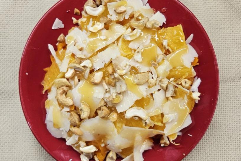 A layered dish of pumpkin, orange, parmesan, and cashews drizzled with honey, presented on a red plate.