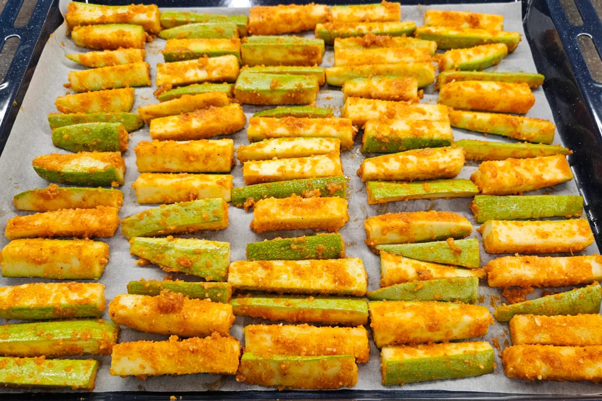 Zucchini sticks arranged evenly on a parchment-lined baking sheet before going into the oven.