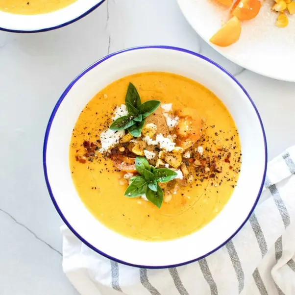 A bowl of baked pumpkin soup, topped with croutons and fresh basil leaves.
