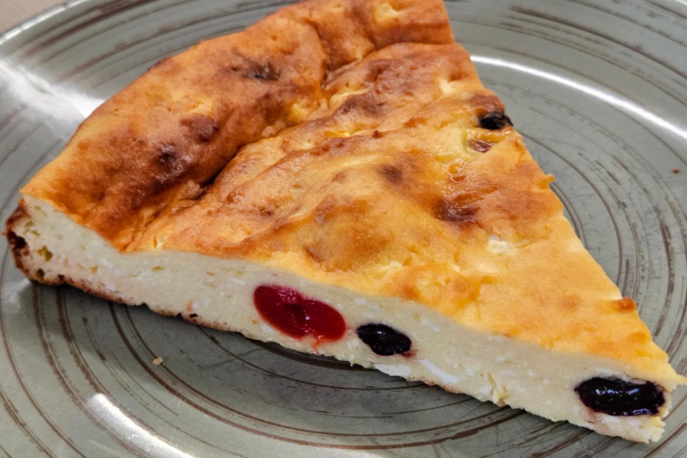 A slice of cottage cheese casserole with raisins and dried cherries on a dark green plate.