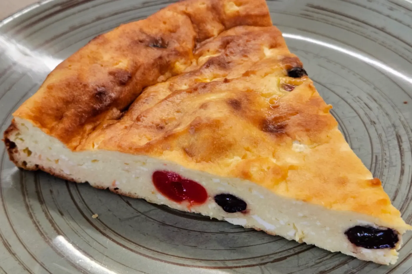 A slice of cottage cheese casserole with raisins and dried cherries on a dark green plate.