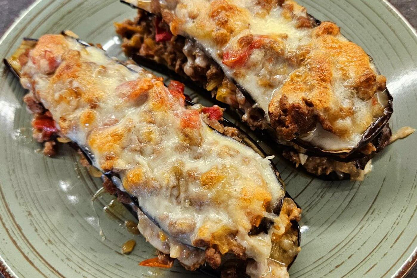 Baked eggplants layered with meat ragu and golden-browned cheese, served on a green-striped plate.