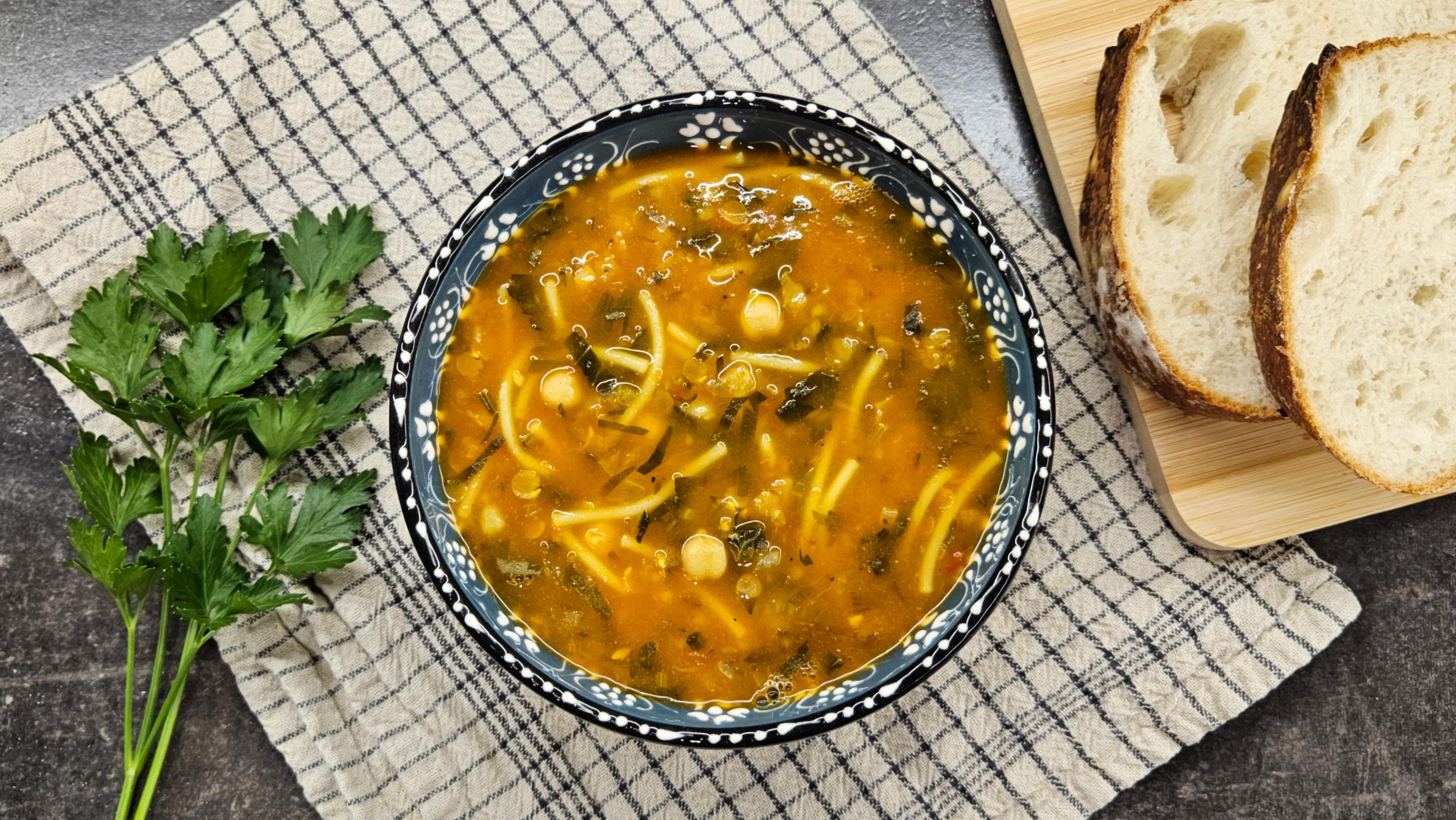 A bowl of Moroccan Harira soup with lentils, chickpeas, herbs, and vermicelli, served with bread slices.