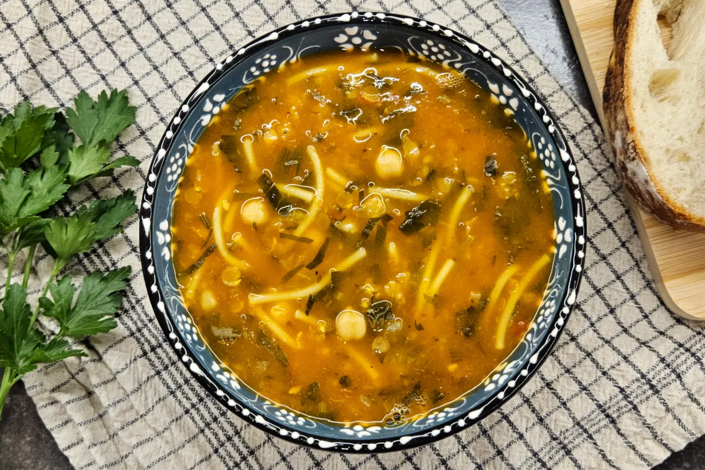 A bowl of Moroccan Harira soup with lentils, chickpeas, herbs, and vermicelli, served with bread slices.