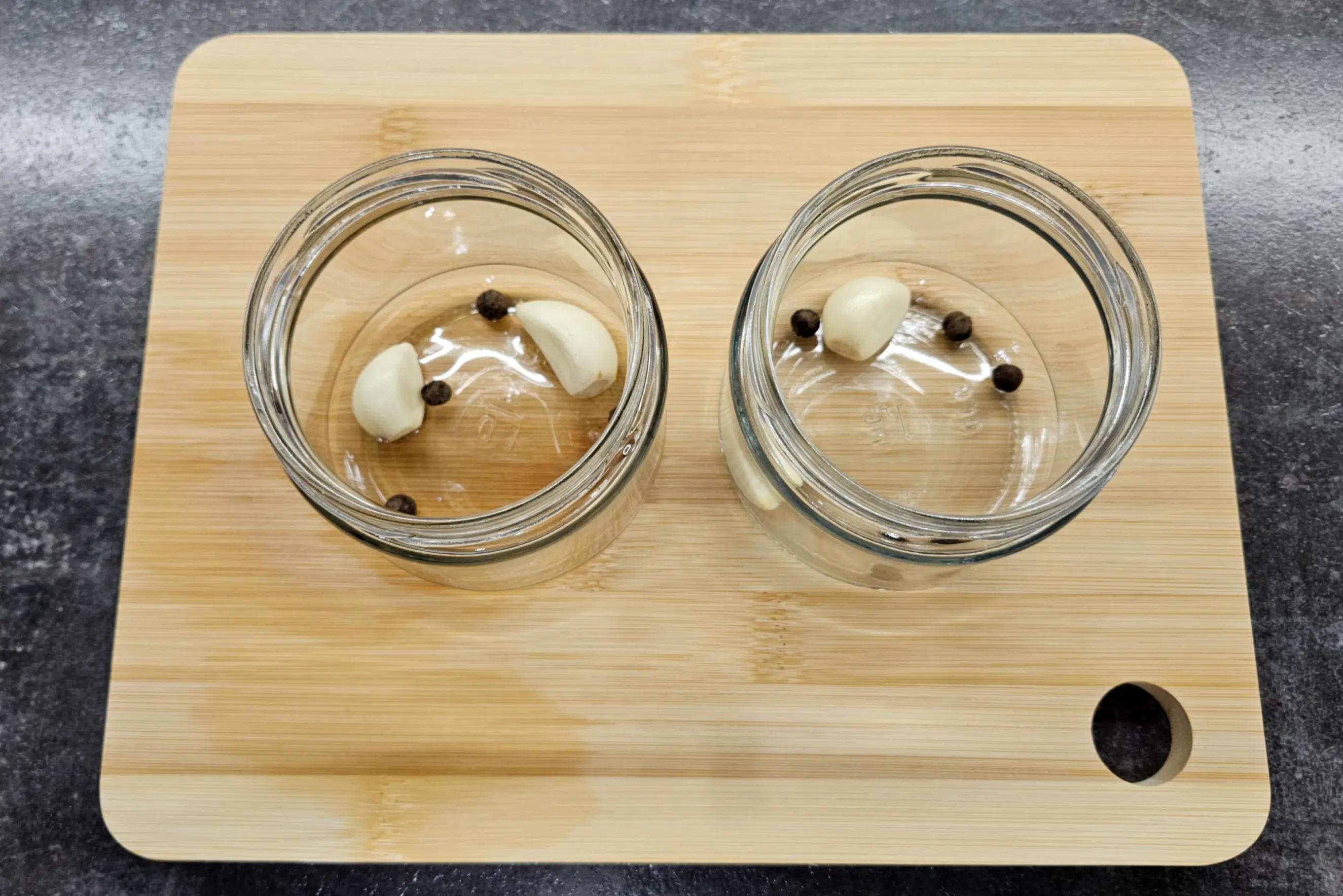 На дно банки викладений часник і горошини чорного перцю.