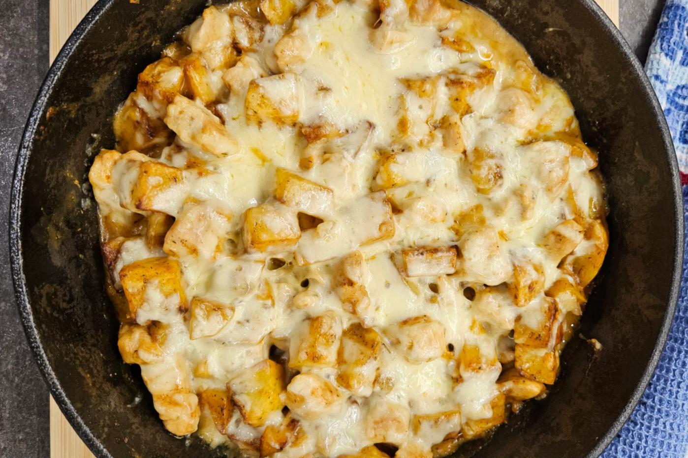 Crispy chicken and potato cubes in a piping hot skillet, generously topped with melted cheese that creates a delicious, golden-brown crust.