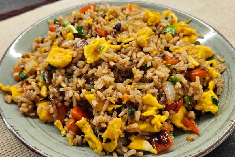 Fried rice with veggies and scrambled egg pieces served on a green ceramic plate.