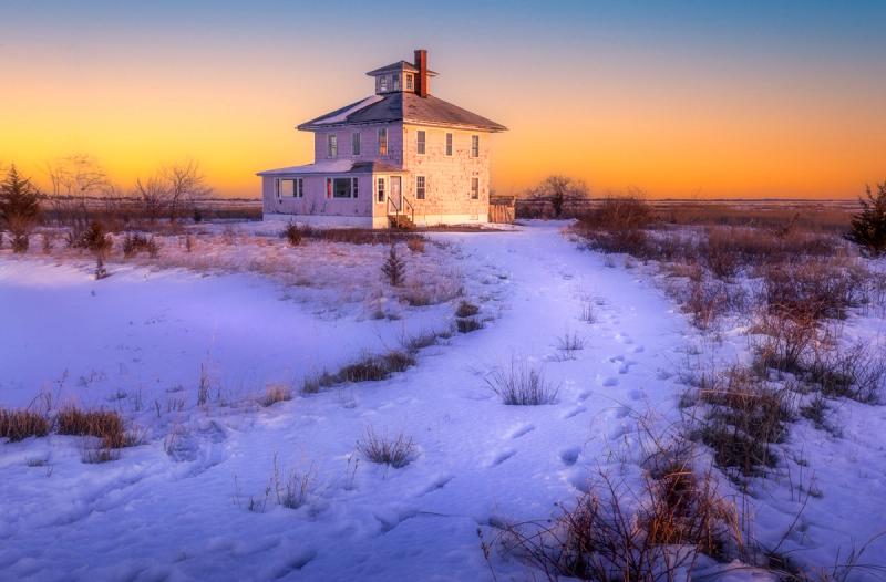 The famous pink house against a pink and blue skies with snow footsteps in the foreground