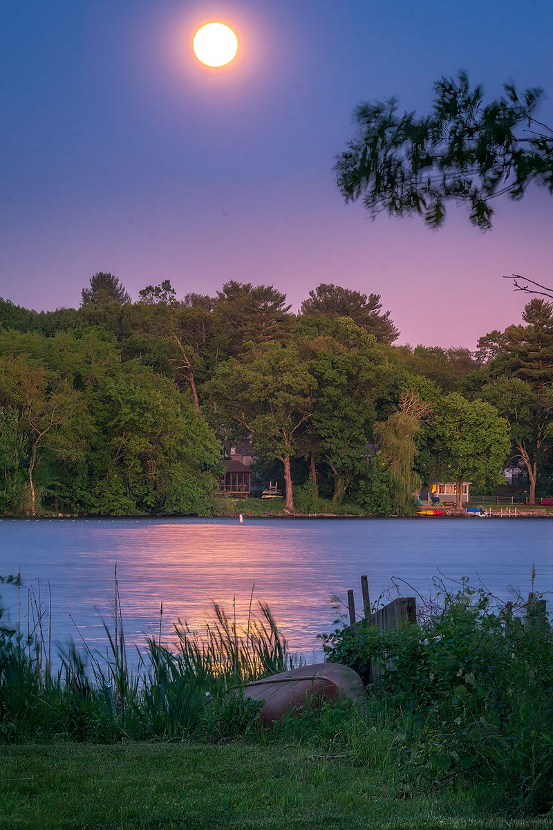 Rising Moon at a lake with golden moonlight reflecting in water and setting magenta glow from the sun