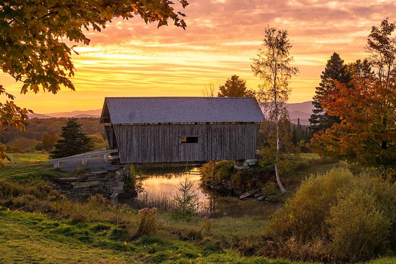 Vermont's famous AM Foster Covered Bridge at sunset against golden skies and fall foliage