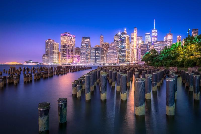 New York City skyline lit up at night from Old Pier One with smooth glassy water