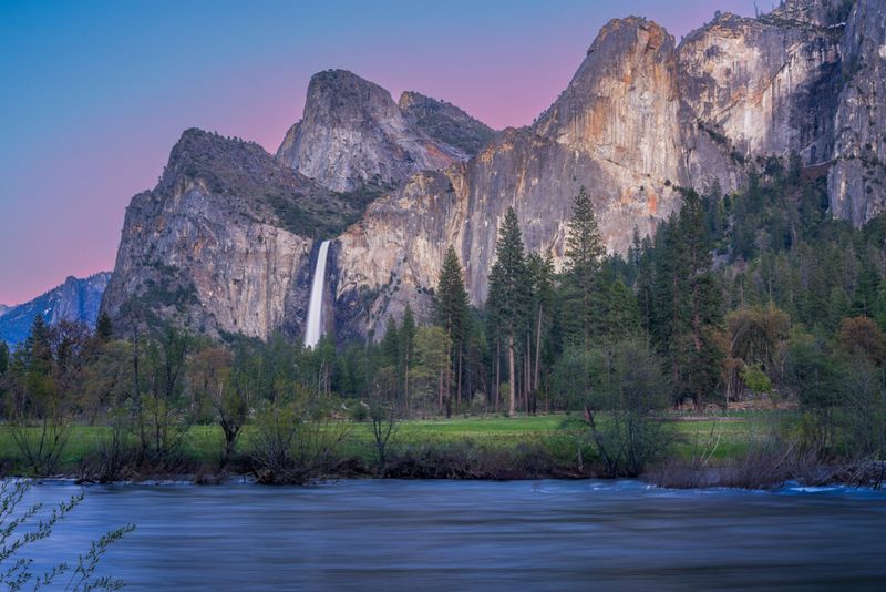 Pink sunrise showing behind mountains in Yosemite Valley with smooth flowing water