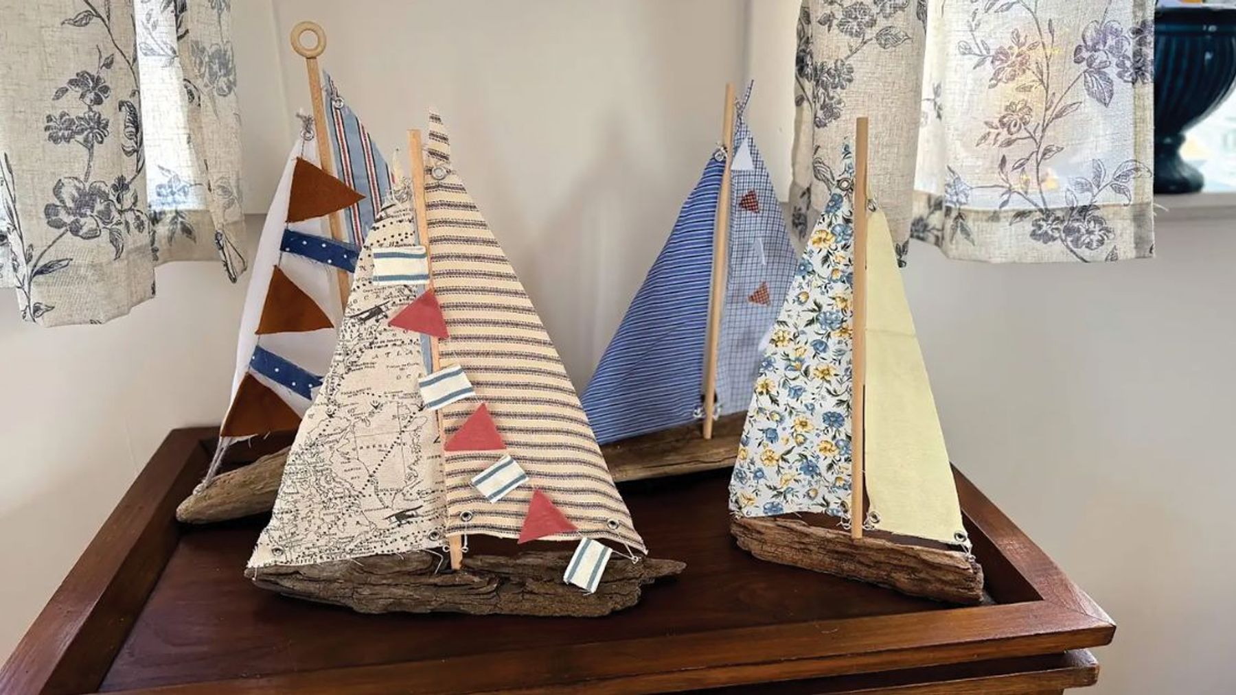 A small handmade sailboat built from driftwood with a fabric sail and twine rigging