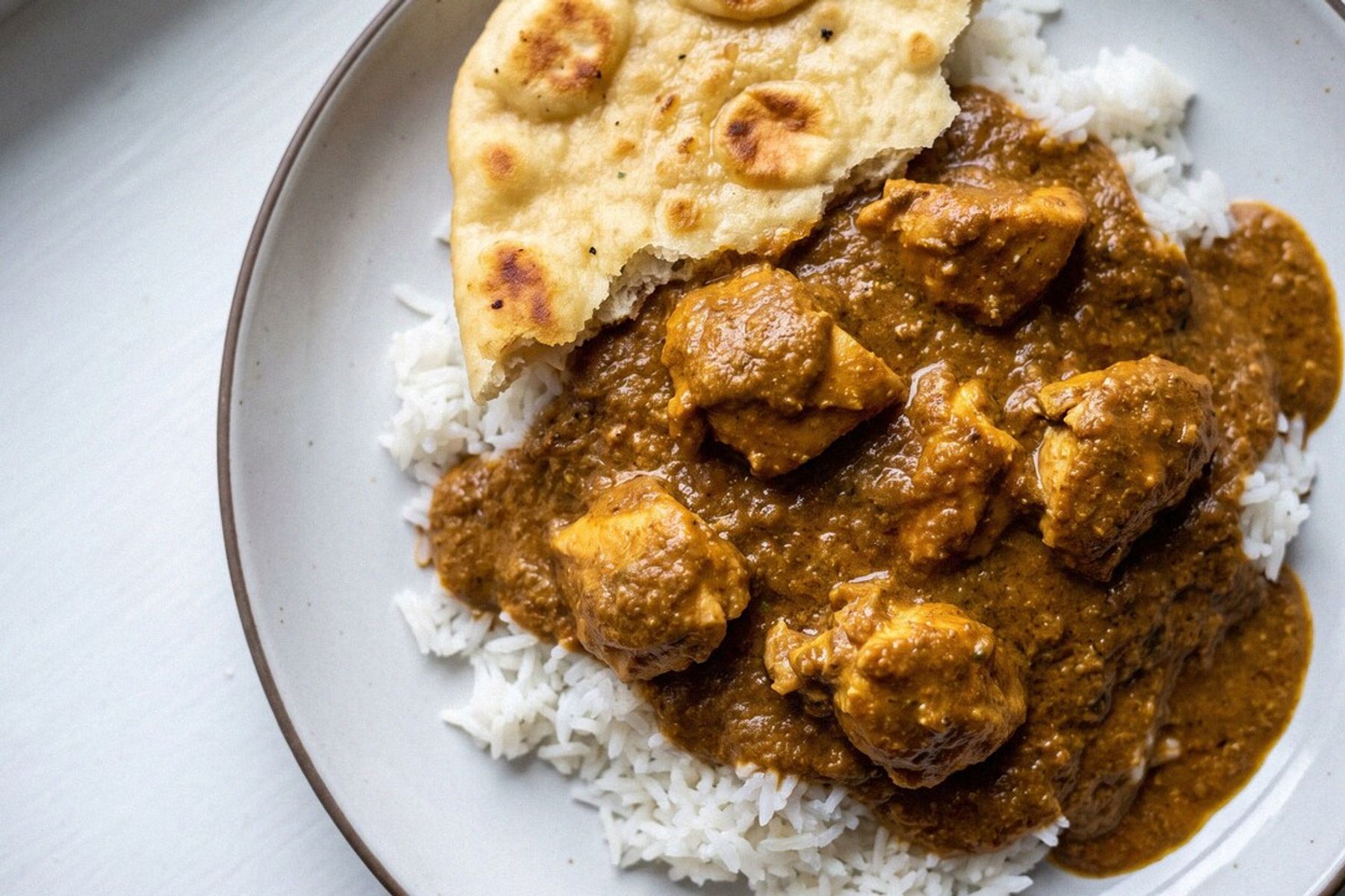 Butter chicken over jasmine rice shot from overhead, a torn piece of golden garlic naan resting at the curry's edge