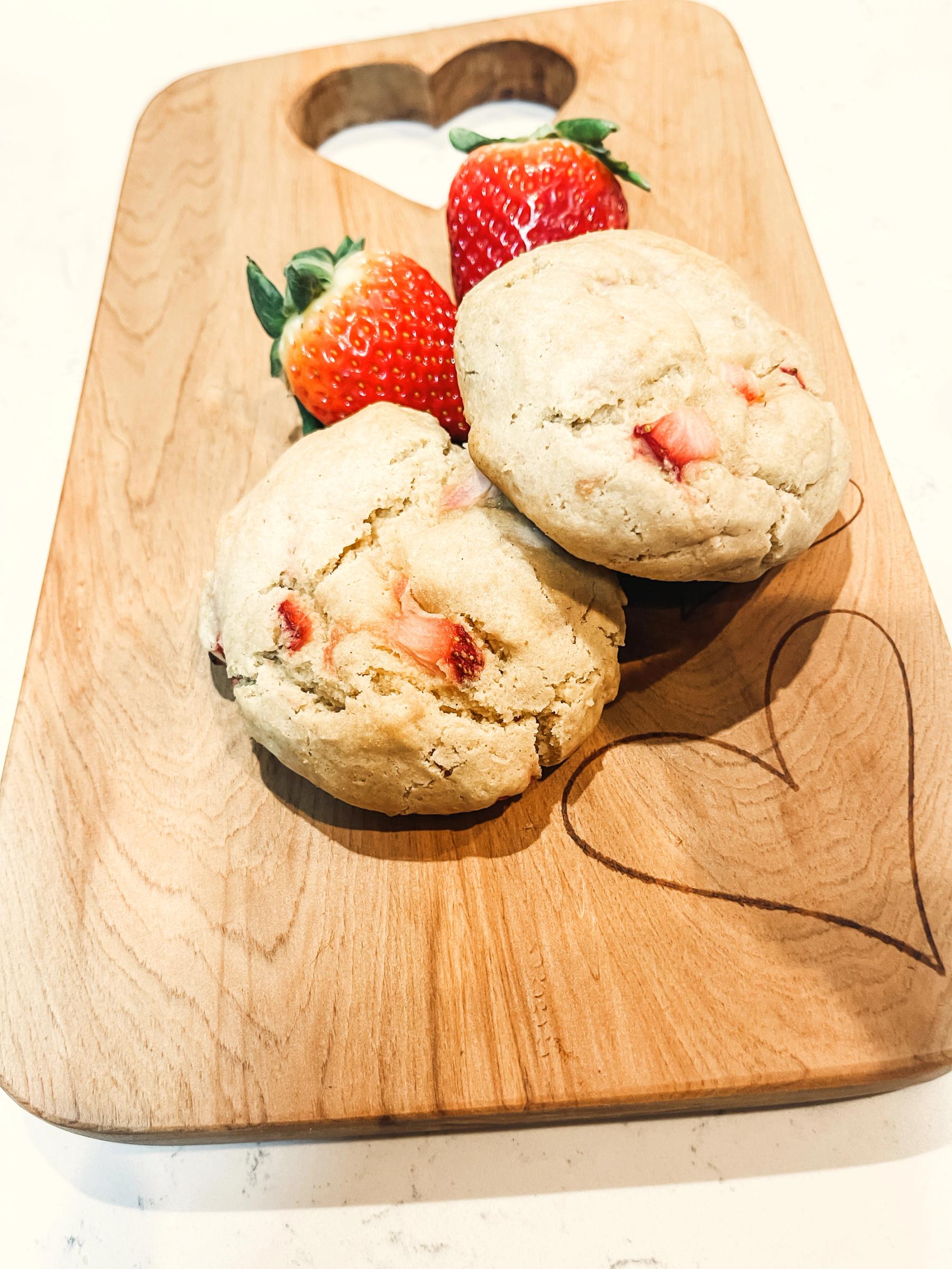 A gluten-free strawberry cheesecake cookie pulled open to show the cream cheese center, with fresh strawberries on a wooden board