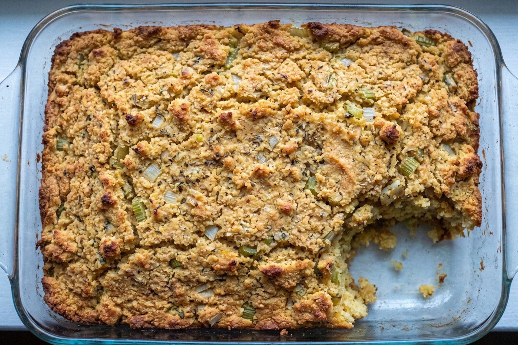 A glass baking dish of golden gluten-free cornbread dressing shot from overhead, one corner scooped out