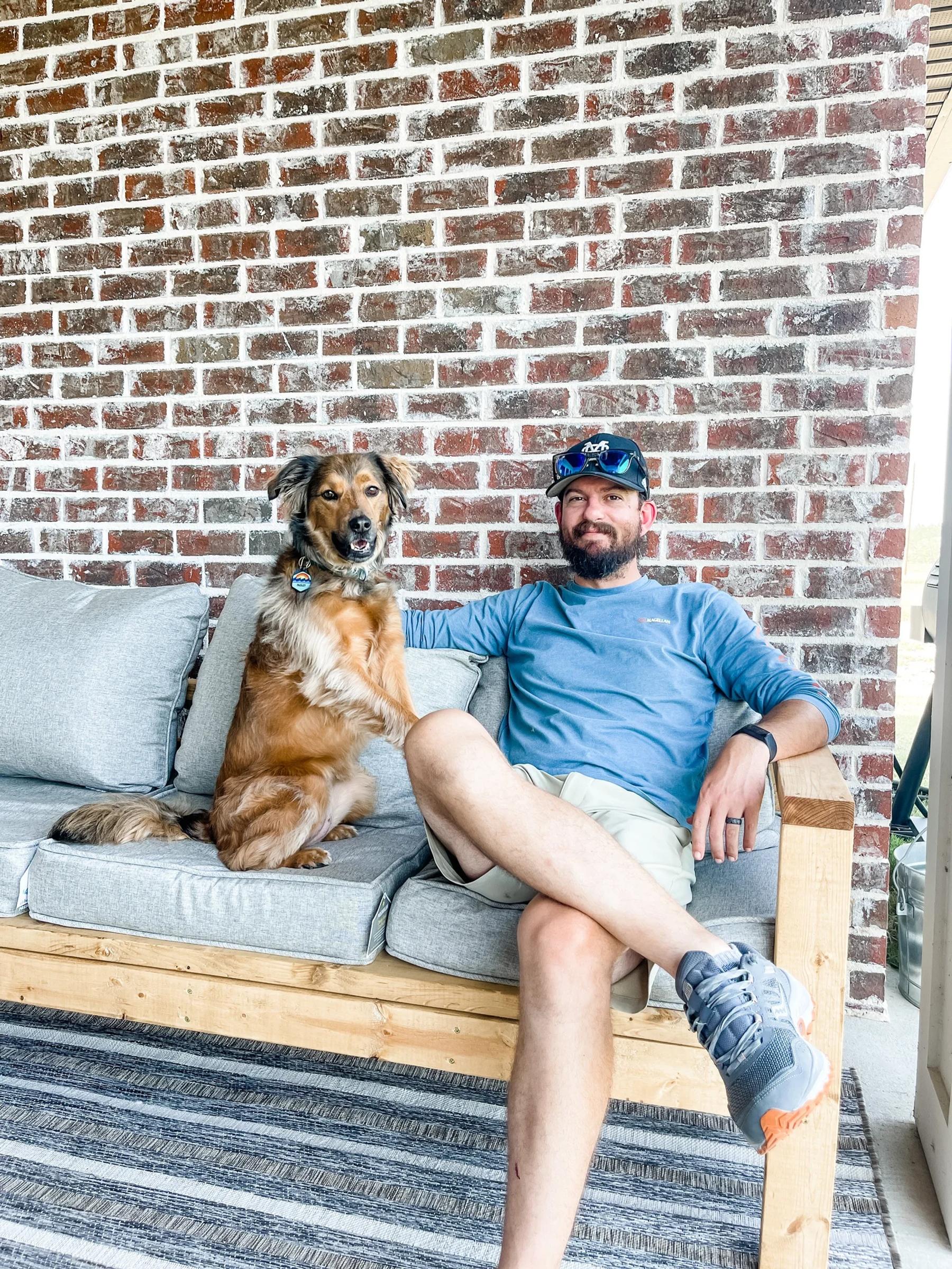 A handmade wood patio couch with gray cushions against a brick wall