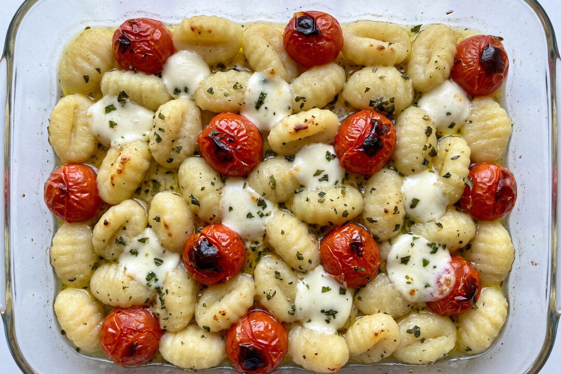 A glass baking dish of three-ingredient gluten-free gnocchi shot from overhead — golden gnocchi, blistered cherry tomatoes and melted mozzarella pearls