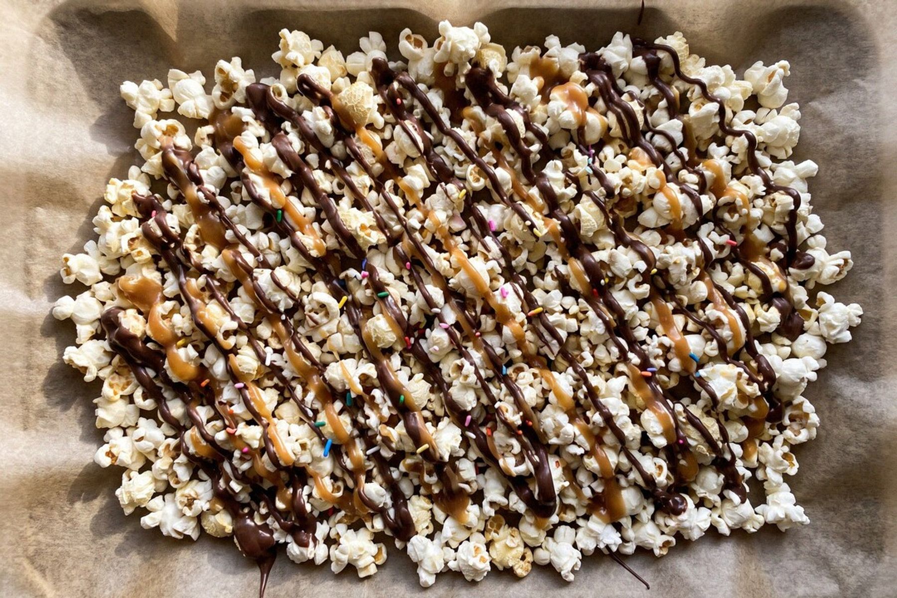 Movie-theater popcorn spread on parchment, drizzled zebra-style with crisscrossing ribbons of chocolate and caramel