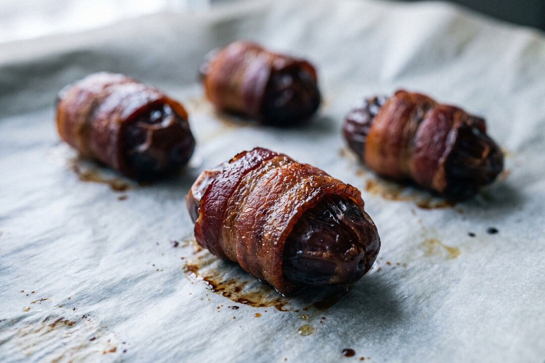 Bacon-wrapped dates fresh out of the oven on crinkled parchment, the bacon baked golden-crisp around the soft dates