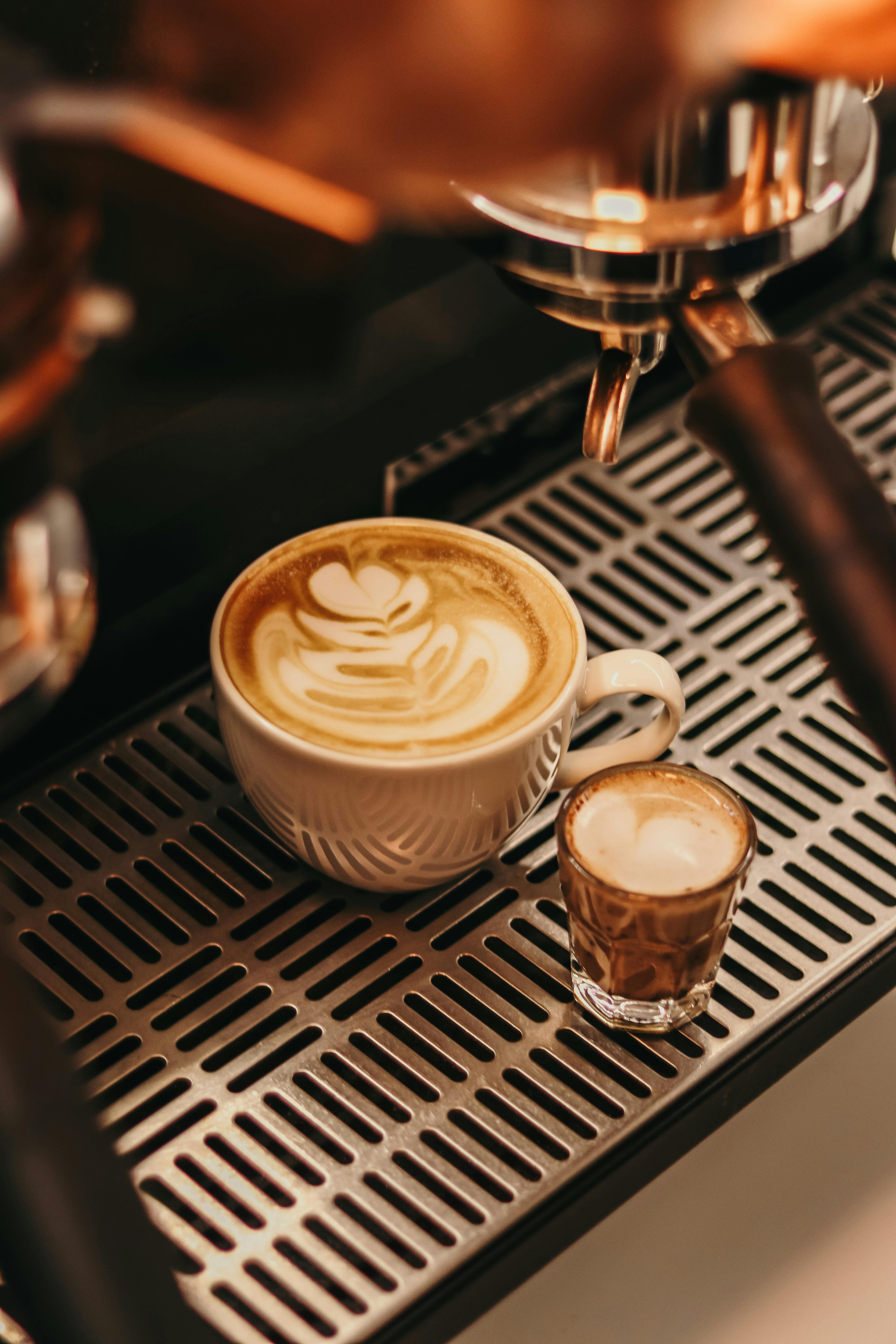A latte with heart latte art and a small espresso shot on a metal grate.