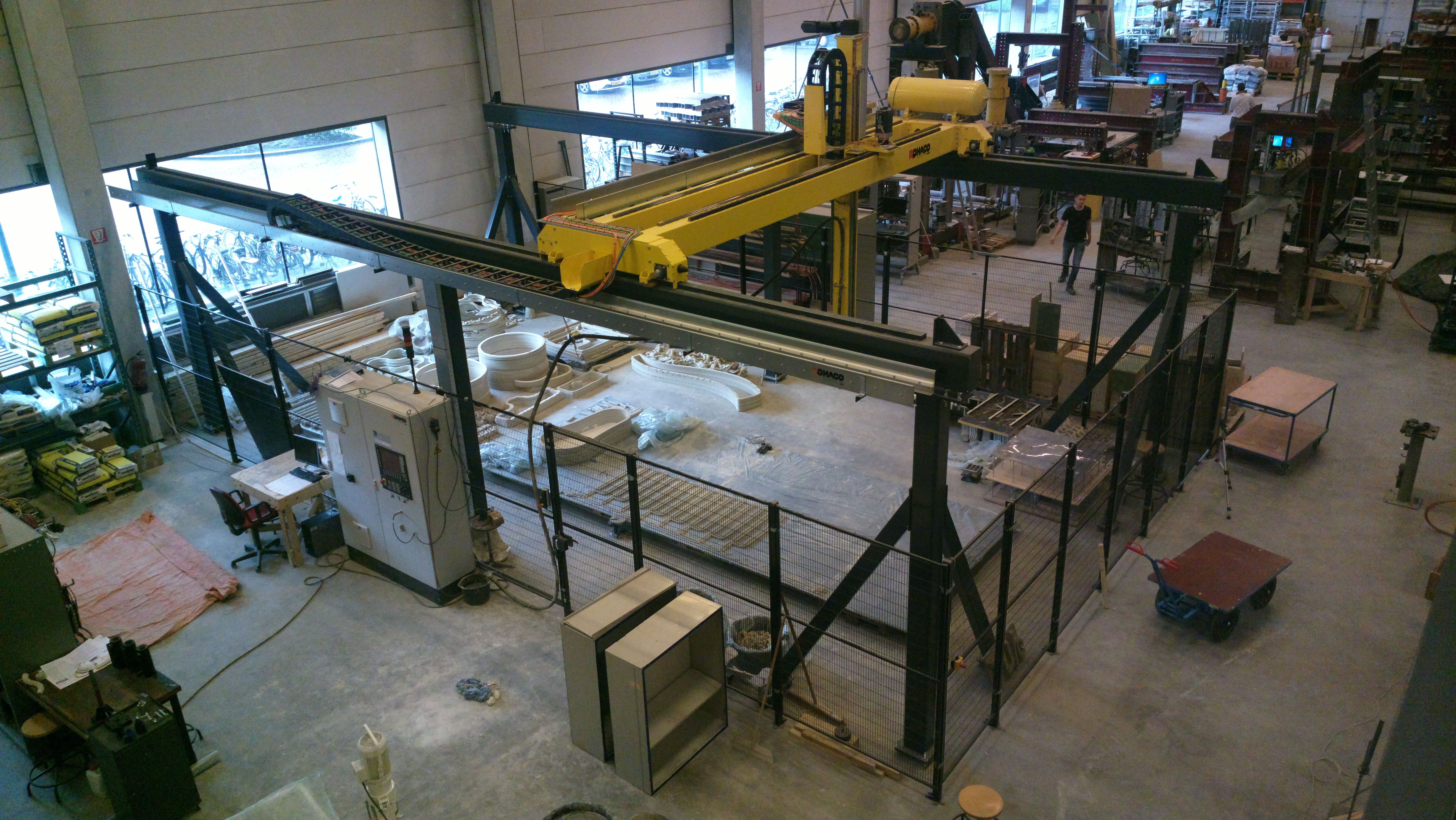 Impressora 3D de grande porte instalada em laboratório, com peças de concreto sobre a área de trabalho.