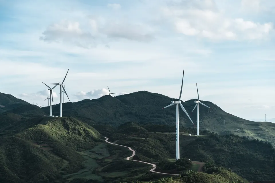 Wind turbines on green hills under a partly cloudy sky.