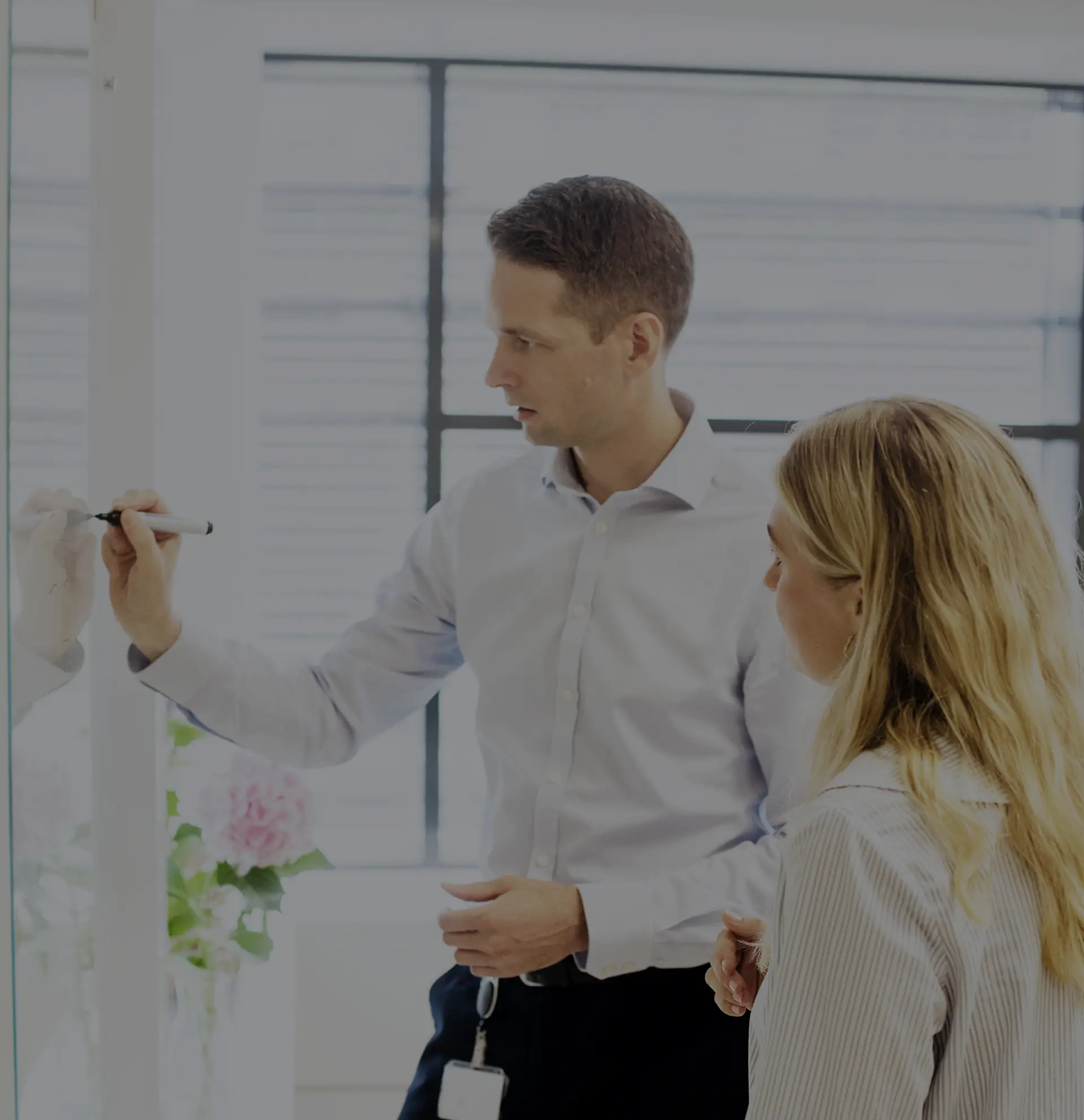 Two people writing on a whiteboard in an office.