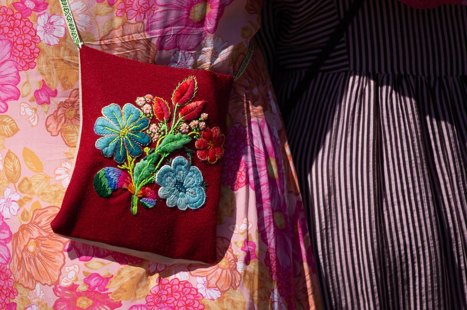 Närbild på en kjolsäck i rött kläde med broderade blommor i blått och rött.